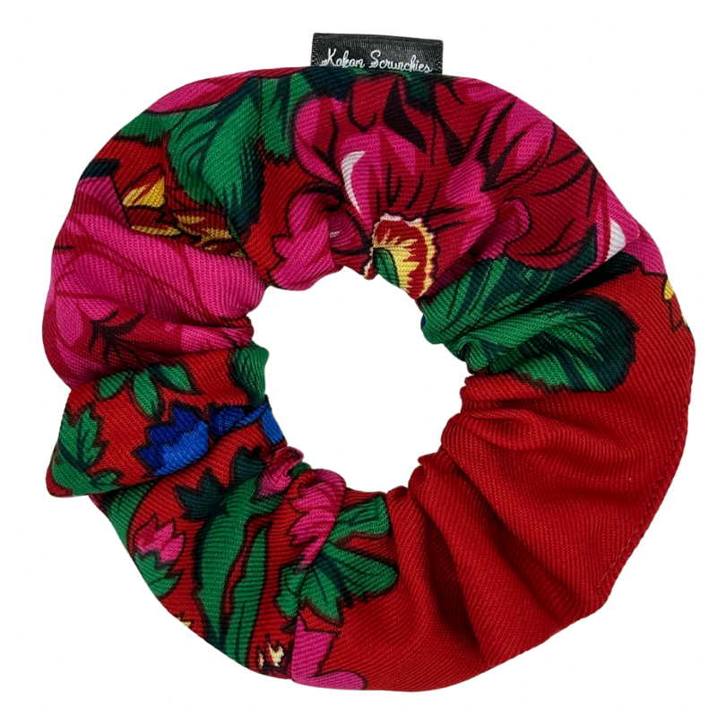 A red scrunchie with a floral pattern, featuring tags with brand name &