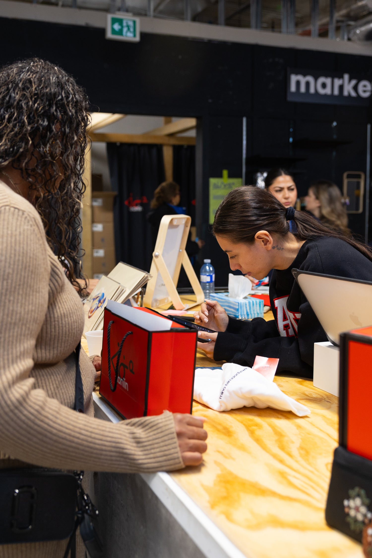 Founder and CEO Chelsee Pettit interacting with a customer at the cashier counter with a branded shopping bag in Aaniin Apparel pop-up store at the Eaton Centre Mall. Photo by Benjamin's Agency Inc.