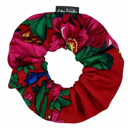 A red scrunchie with a floral pattern, featuring tags with brand name &