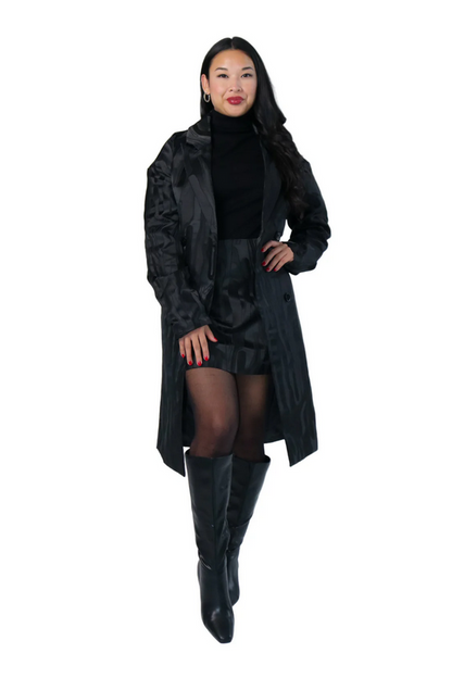 Woman wearing a long black coat, black dress, and black knee-high boots on a white background