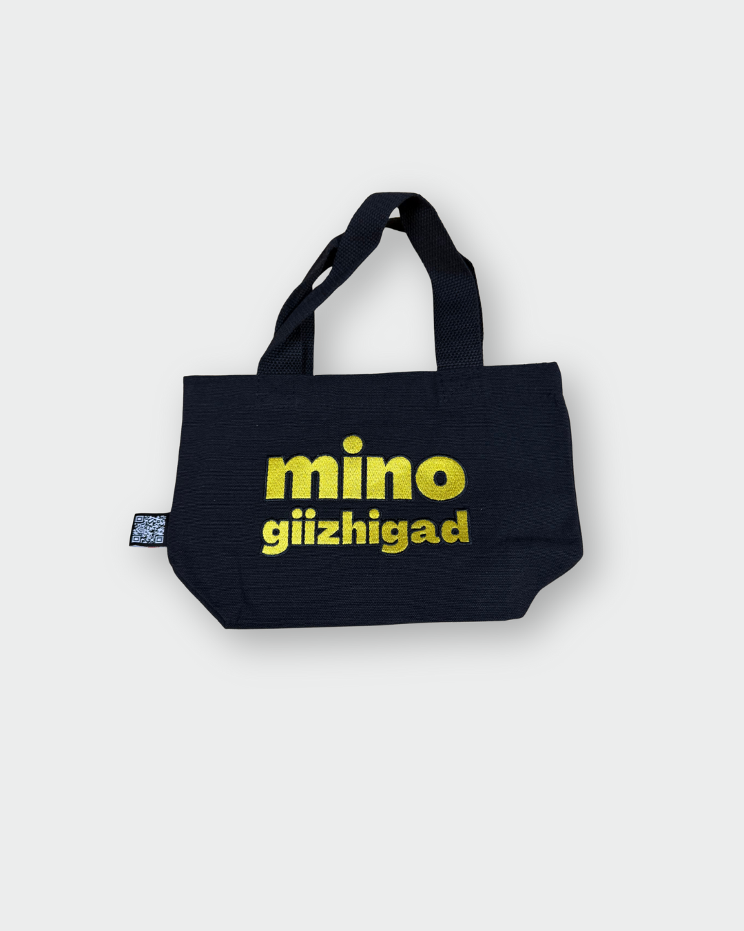 the back side of a black Mino giizhigad tote bag with a yellow smiley face design on a white background