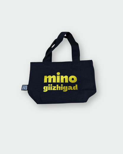 the back side of a black Mino giizhigad tote bag with a yellow smiley face design on a white background