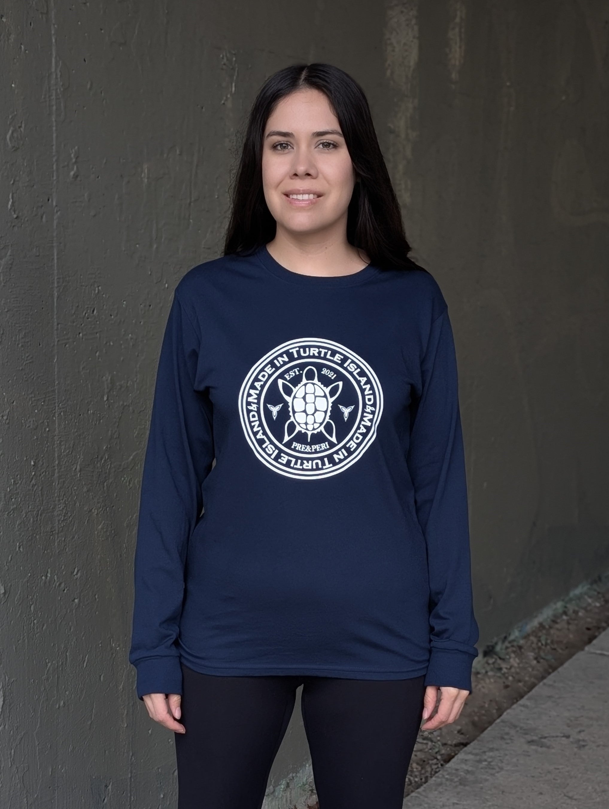 A woman wearing a navy long sleeve t-shirt with a white print of a turtle in the centre of a circle with words &quot;Made in Turtle Island&quot; around it twice