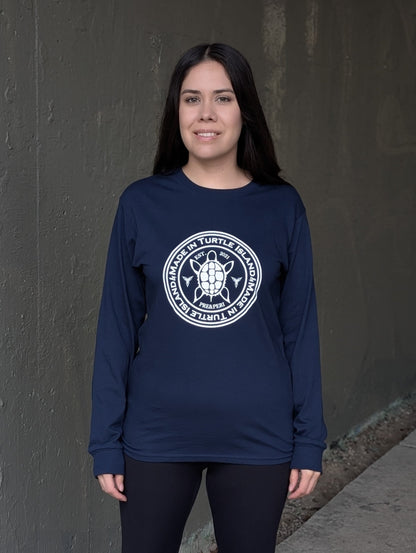 A woman wearing a navy long sleeve t-shirt with a white print of a turtle in the centre of a circle with words &quot;Made in Turtle Island&quot; around it twice