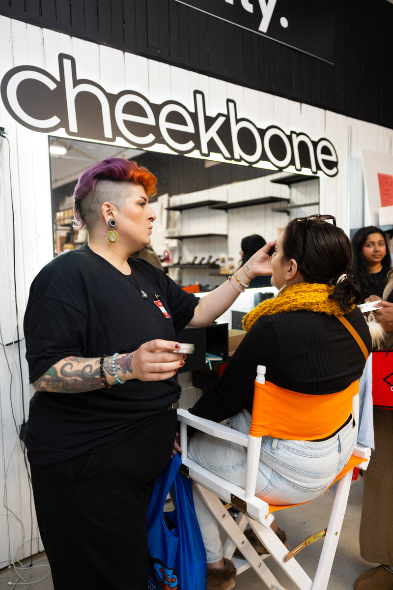 Person getting a makeover in front of a 'Cheekbone' beauty station at aaniin pop-up store.