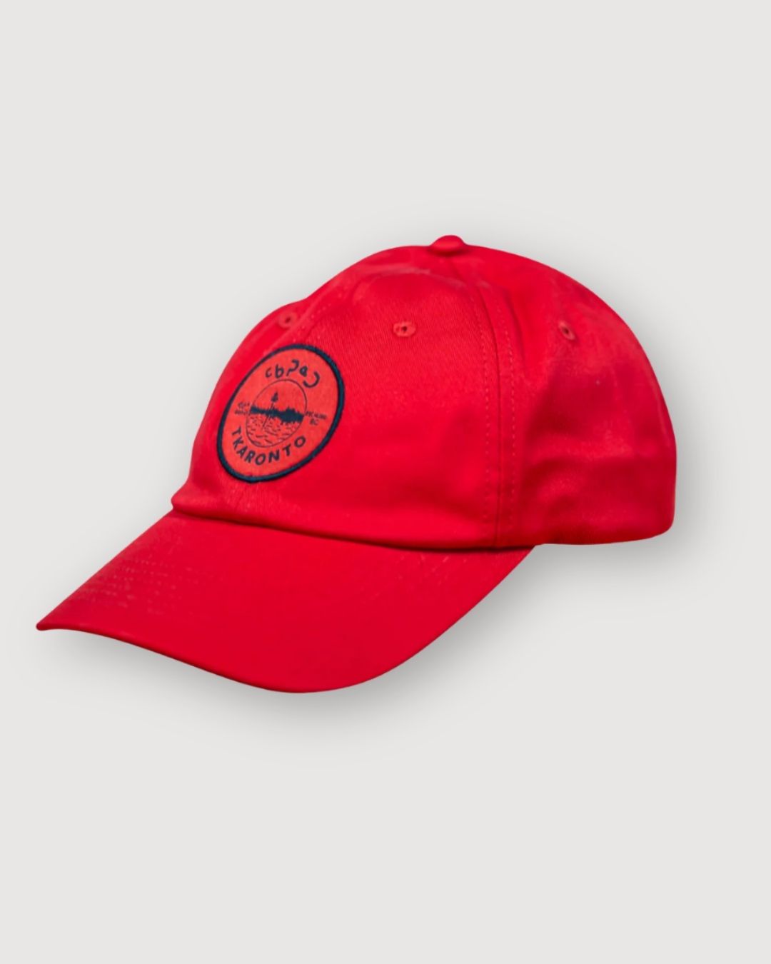 Red aaniin dad cap, side view, with the tkaronto crest on it in black to resemble the Toronto sports teams that use red and black